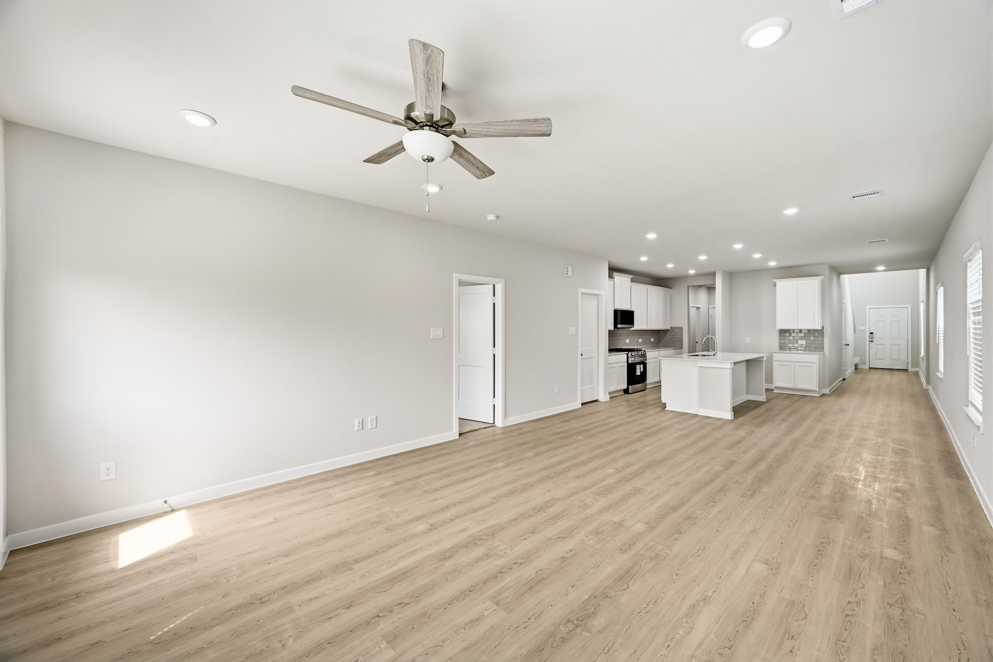 A large empty room with a ceiling fan and a wood floor.