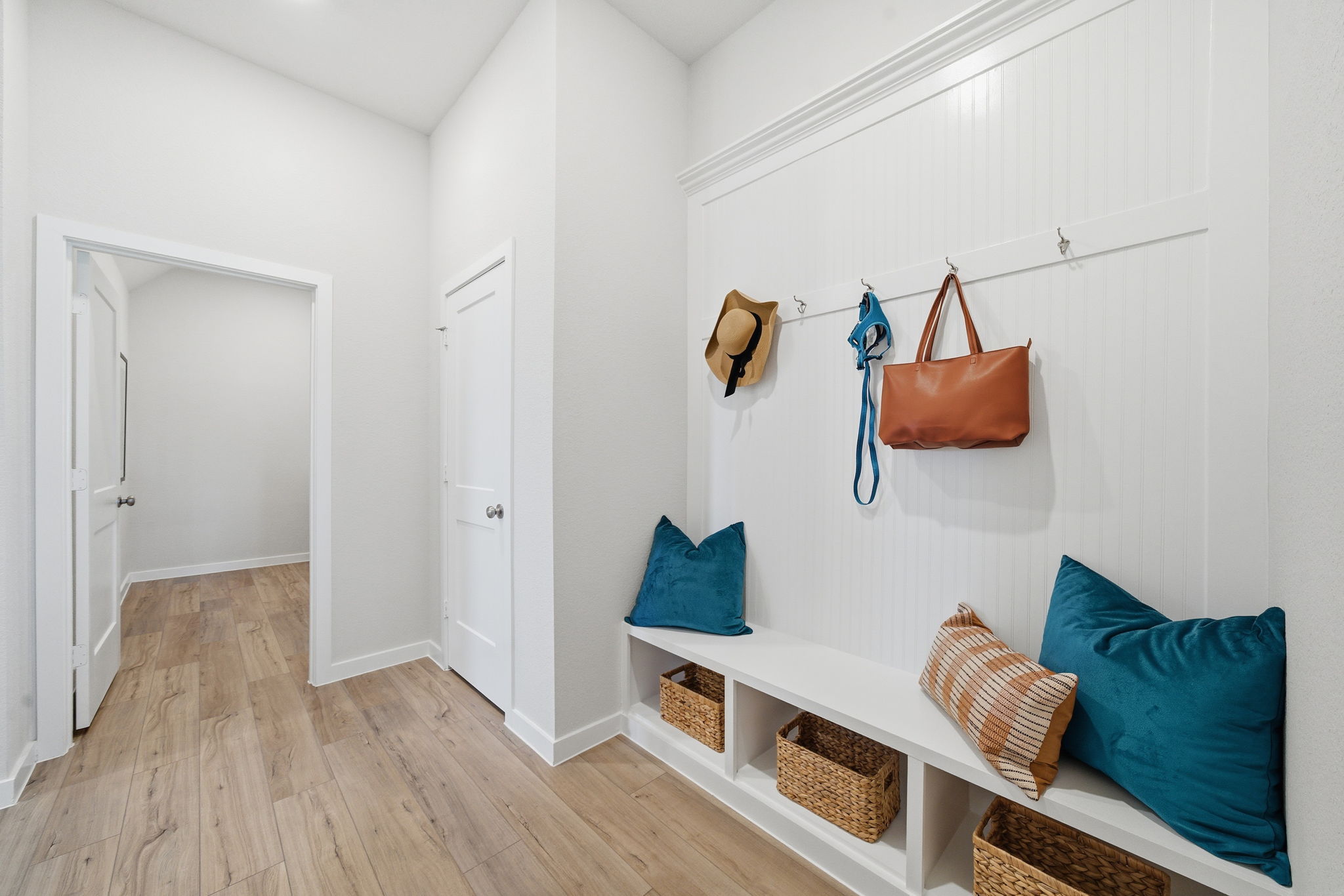 A room with a wood floor and a white wall with a blue pillow and a basket and a.