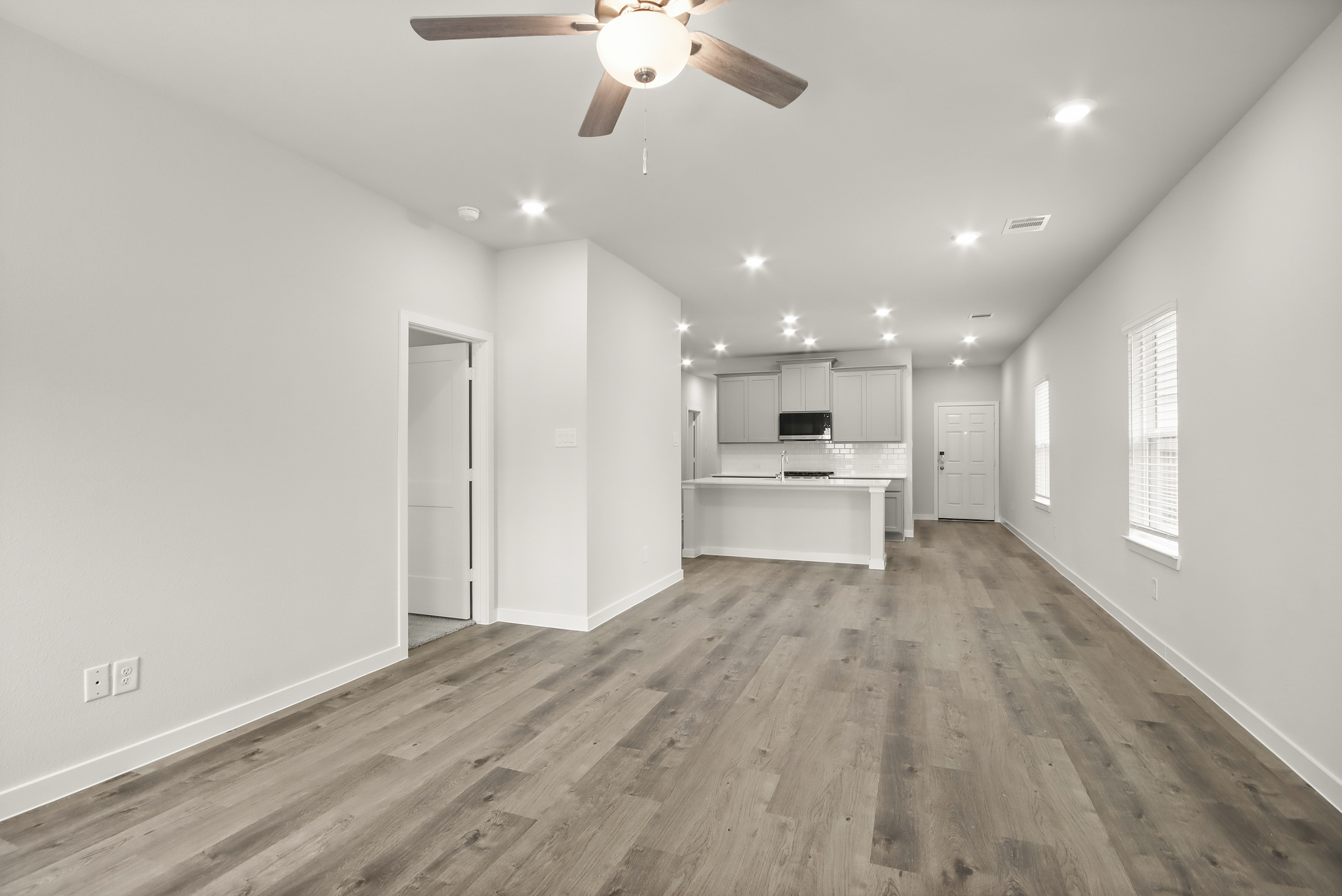 A large empty room with a ceiling fan and a wood floor.