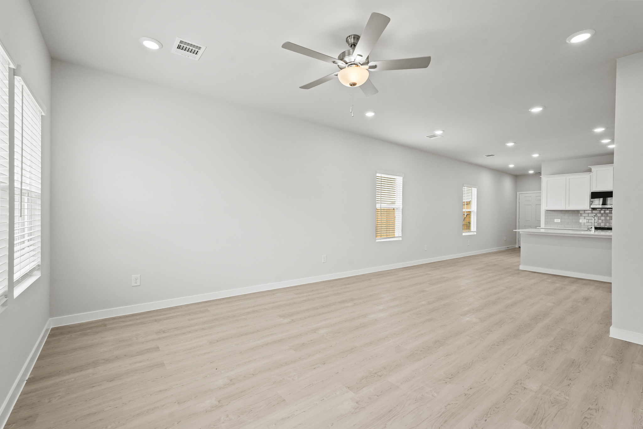 A large empty room with a ceiling fan and a wood floor.