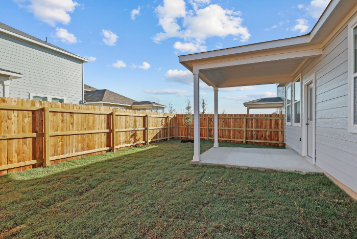 A fenced in yard with a house and a grass yard.